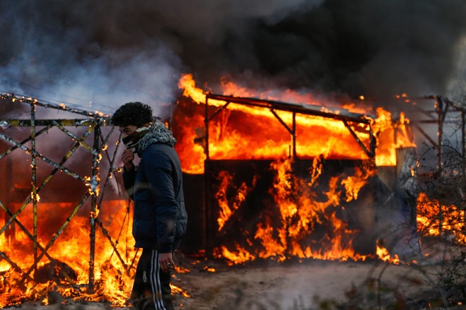 A migrant watches a shelter burn in Monday during the start of the government effort to pull down part of the eJunglef migrant camp in Calais, France, on the English Channel.